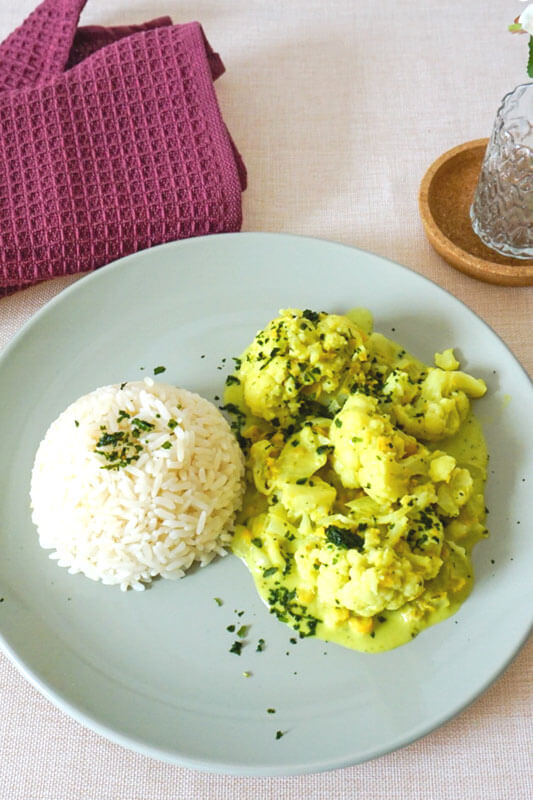 Blumenkohl-Kicherernsen-Curry auf blauem Teller mit Reis als Beilage steht auf Tisch