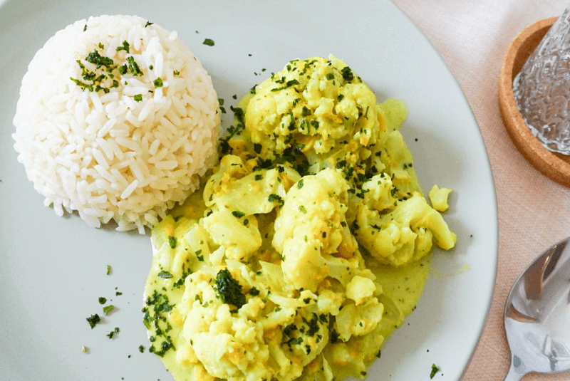 Blumenkohl-Kicherernsen-Curry auf blauem Teller mit Reis als Beilage steht auf Tisch